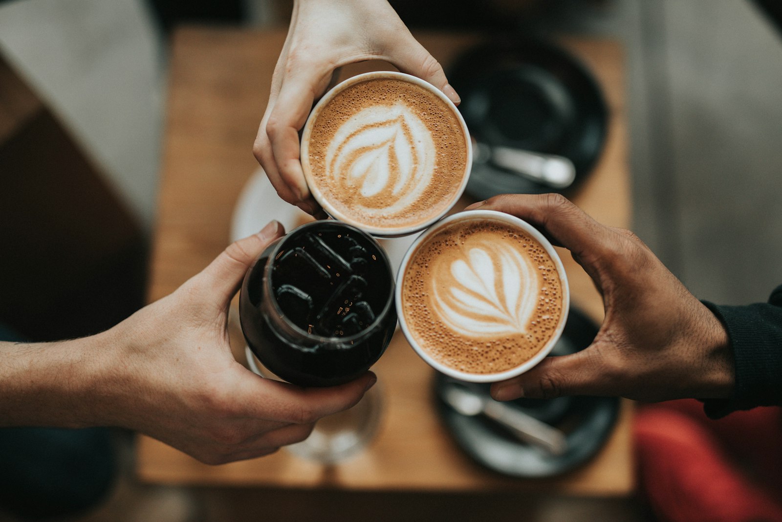 Steaming cappuccino served in stacked white cups beside roasted coffee beans.
